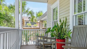 A wooden porch with white railings, two rocking chairs, and a potted plant.