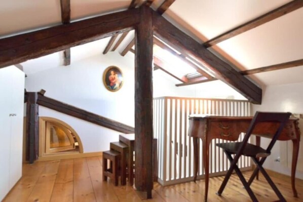 A room with exposed wooden beams, a wooden floor, a desk with a chair, and a small staircase leading to another level. - ATTICO SAVORGNAN (Venice)