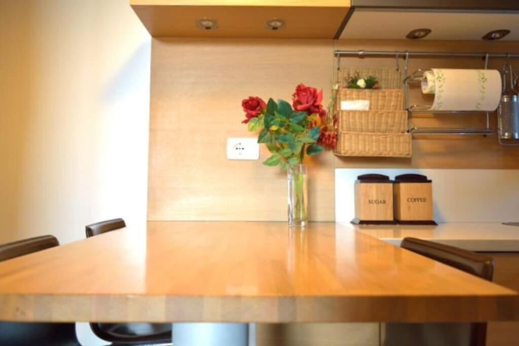 Une table en bois sur laquelle se trouvent un vase de fleurs, un panier et deux récipients étiquetés « SUCRE » et « CAFÉ ».