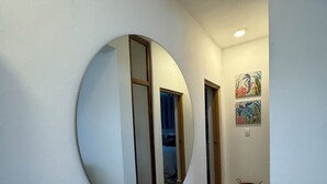Un couloir avec un grand miroir rond accroché au mur, des portes en bois et un petit panier posé sur le sol.