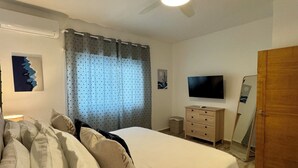 Une chambre à coucher avec un lit, un ventilateur de plafond, une télévision, une commode et une porte.