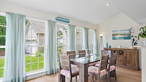 A dining area with a glass table, wooden chairs, and light blue curtains. - Spacious 4-bedroom Single home in Ocean View with large outdoor spaces and Pool! (Ocean View)