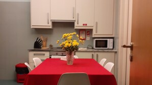 Uma sala de jantar com toalha vermelha, cadeiras brancas, um vaso com flores amarelas e armários brancos.