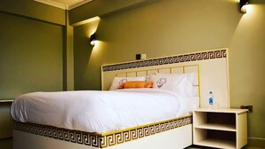 Un lit avec une tête de lit blanche ornée d’un motif décoratif, une table de chevet avec une bouteille, et un luminaire fixé au mur.