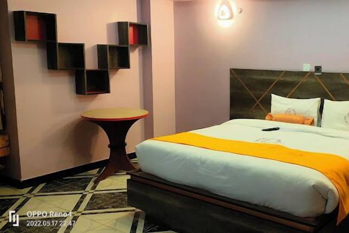 Una habitación de hotel con una cama, una mesita de noche, una pequeña mesa redonda y estantes en la pared.
