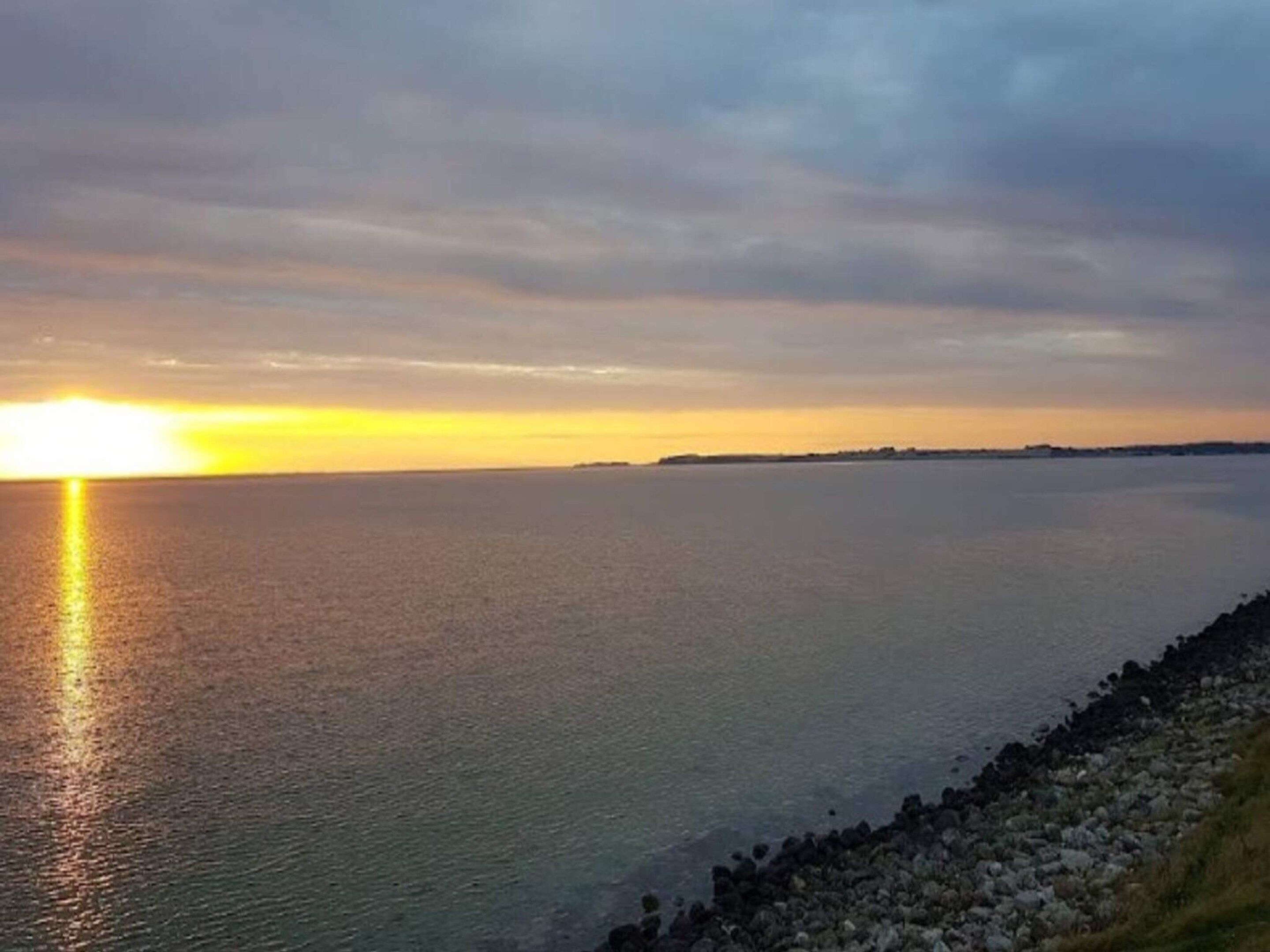 Un atardecer costero con aguas tranquilas reflejando el cielo.