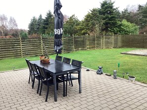 A patio with a black table and chairs, surrounded by a wooden fence and greenery. - 7 Person Holiday Home in Vaeggerlose (Vaeggerlose)