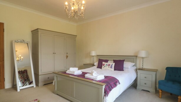 A bedroom with a bed, nightstands, a dresser, a mirror, and a chandelier. - Glasfryn (Caernarfon)