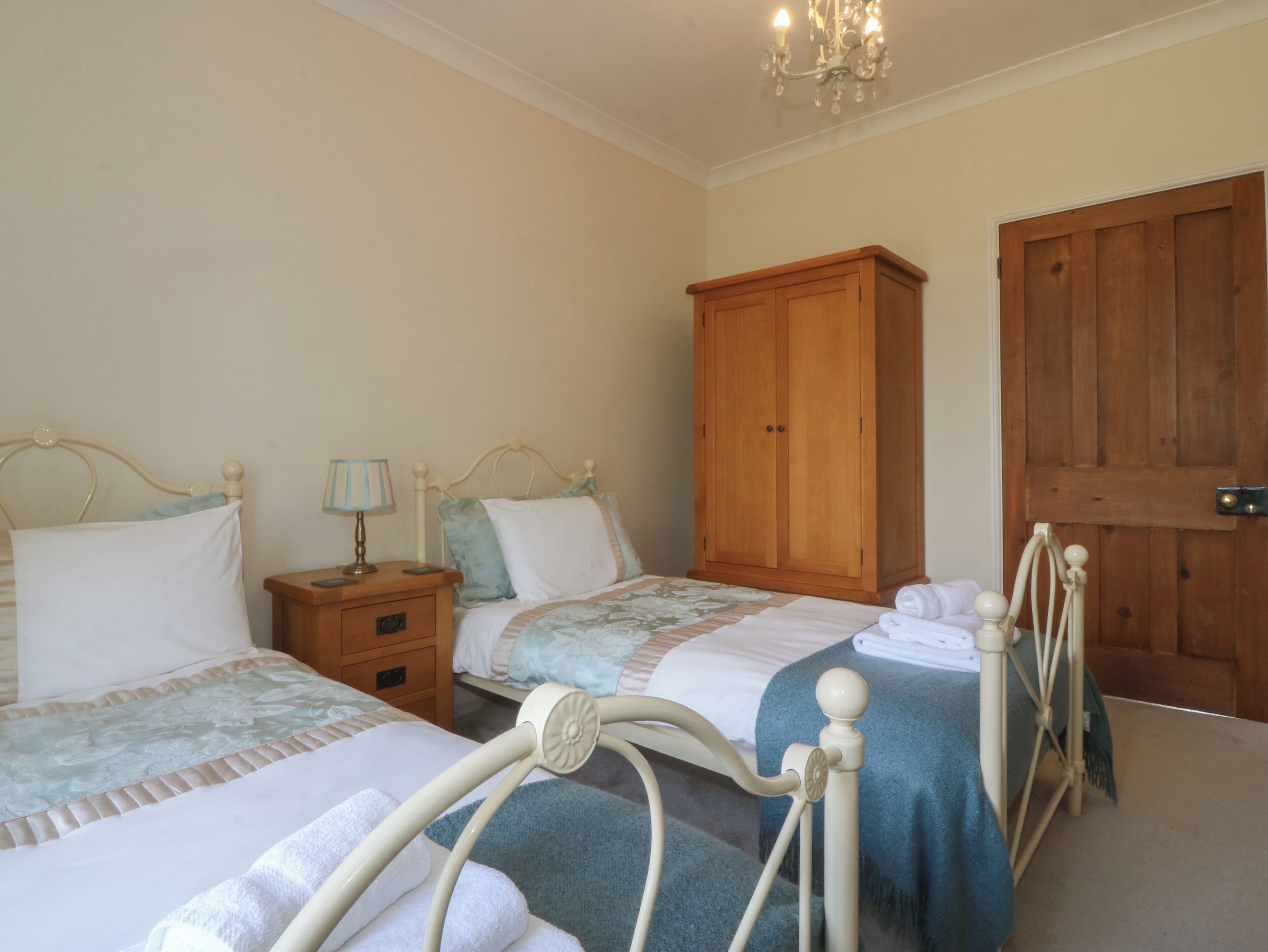 A bedroom with two beds, wooden wardrobe, and a chandelier.