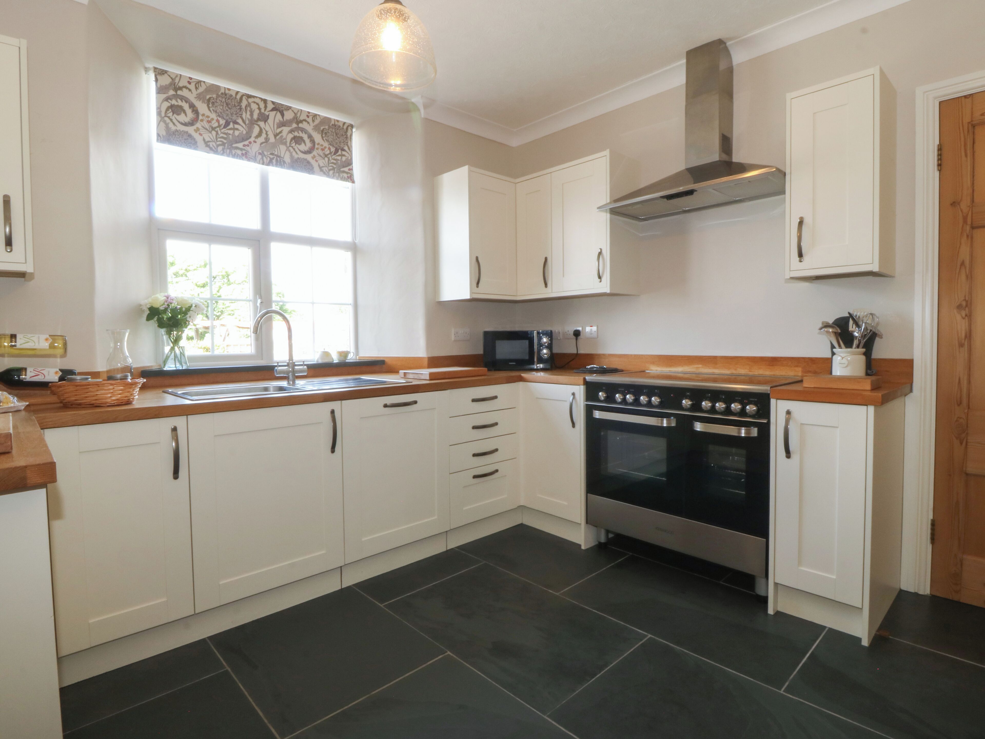 A kitchen with white cabinets, a black stove, and a window with a floral curtain.