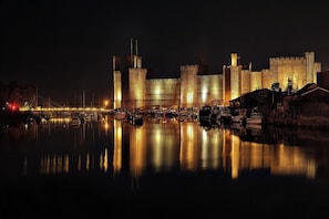 A historic castle with a moat, illuminated by lights, reflecting on the water. - Glasfryn (Caernarfon)
