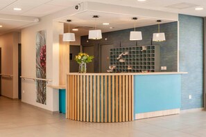 A reception area with a wooden reception desk, a blue accent wall, and a shelf with magazines. - Quality Aparthotel Mont-de-Marsan (Mont-de-Marsan)