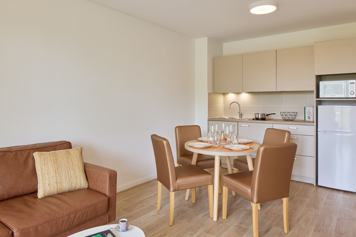 A modern kitchen with a dining area, including a brown leather sofa, a round table with chairs, and a white refrigerator.