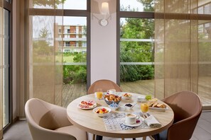 A breakfast table with croissants, fruits, and juice, set on a balcony with a view of a building and greenery. - Quality Aparthotel Mont-de-Marsan (Mont-de-Marsan)
