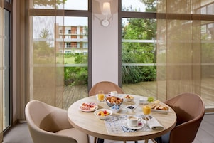 Una mesa de desayuno con cruasanes, frutas y jugo, ubicada en un balcón con vista a un edificio y follaje.
