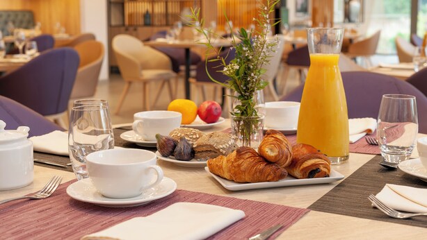 Une table dressée pour le petit-déjeuner, avec des croissants, des fruits et un verre de jus d’orange.