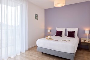 A bedroom with a bed, two bedside lamps, a nightstand, a hat, and sunglasses on the bed.