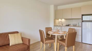 A modern kitchen with a dining area, including a brown leather sofa, a round table with chairs, and a white refrigerator.