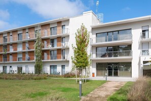 Un immeuble résidentiel moderne à plusieurs étages, doté de balcons, de grandes fenêtres et d’une cour verdoyante.