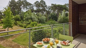Un balcon avec une table préparée pour le petit-déjeuner, comprenant des croissants, des fruits et du jus, donnant sur un jardin luxuriant.
