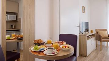 A modern hotel room with a dining area featuring breakfast items, a television, and a comfortable seating arrangement.