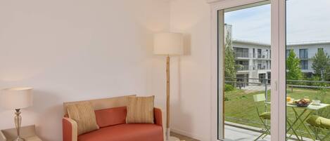 Uma sala de estar moderna com um sofá vermelho, um abajur e vista para uma varanda com mobiliário exterior.