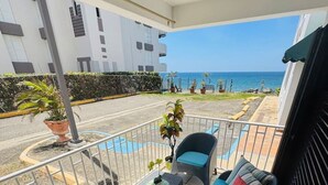 Een balkon met twee rieten stoelen en een kleine tafel, met uitzicht op een straat en de oceaan.