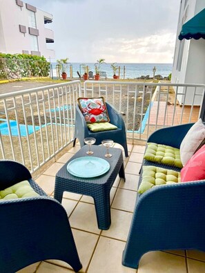 An outdoor seating area with chairs and a table, a small pool, and a view of the sea.