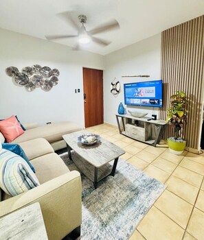 A living room with a sofa, coffee table, TV, and decorative items. - Serenity Sanctuary | Walk to Beach Retreat (Rincón)
