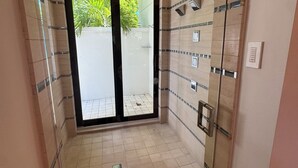 A modern bathroom with a glass shower enclosure, tiled floor, and a door leading to an outdoor area.