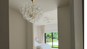 A modern bedroom with a large bed, a ceiling fan, and a view of greenery outside.