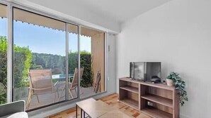 A modern living room with a large sliding glass door leading to a balcony, a wooden TV stand, and a small table. - Apartment with view on the golf of Houlgate (Houlgate)