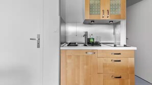 A compact kitchen with wooden cabinets, a stainless steel countertop, and a built-in oven. - Apartment with view on the golf of Houlgate (Houlgate)