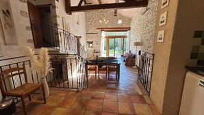 A rustic interior with a stone wall, a dining area with a table and chairs, a staircase with a railing, and a view of the outdoors. - Spacious grange - Domaine de Gargoris (Pont-du-Casse)