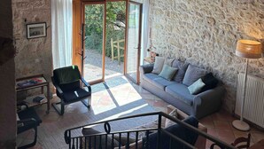 A cozy living room with a stone wall, a wooden ceiling, and a chandelier. There is a sofa, a chair, and a table with a lamp. - Spacious grange - Domaine de Gargoris (Pont-du-Casse)