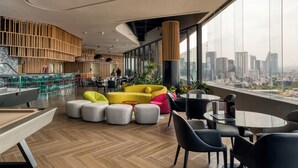Een moderne zithoek met stadszicht, met een gele bank, grijze poufs en zwarte stoelen.