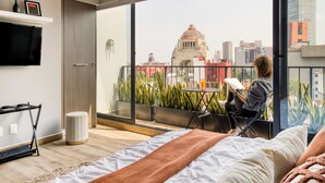 Een moderne slaapkamer met een groot raam, een bed, een televisie en een balkon met uitzicht op de stad.