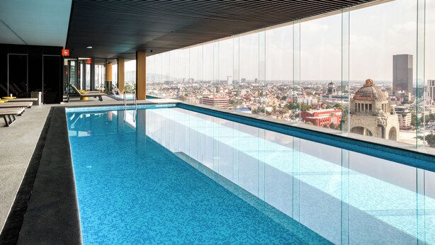 Een modern binnenzwembad met stadszicht, met een glazen balustrade en een eigentijds dakontwerp.