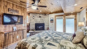 Ein gemütliches Schlafzimmer mit einem großen Bett, einem Kamin, einem Fernseher und einem Deckenventilator.