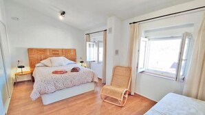 A bedroom with a wooden headboard bed, a bedside table with a lamp, a wicker chair, and a window with curtains. - CERRO LUNA HOUSE (Constantina)