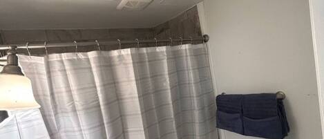 Een badkamer met douchegordijn, toilet, handdoekhouder en prullenbak.