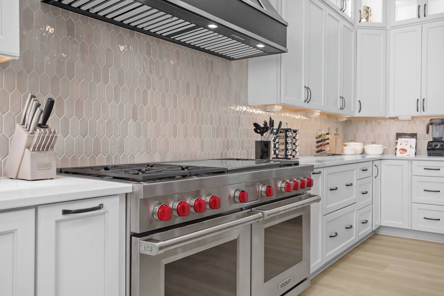 A kitchen with a stainless steel stove, white cabinets, and a hexagonal tile backsplash.