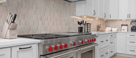 A kitchen with a stainless steel stove, white cabinets, and a hexagonal tile backsplash.
