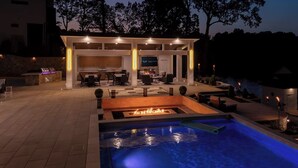 Ein Außenpoolbereich mit Feuerstelle, Sitzgelegenheiten und einer überdachten Terrasse mit Fernseher.
