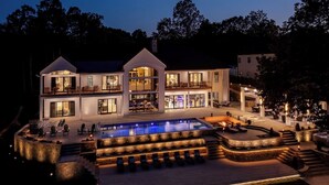 Ein mehrstöckiges Haus mit Schwimmbecken, Außenmöbeln und einem gut beleuchteten Patio.