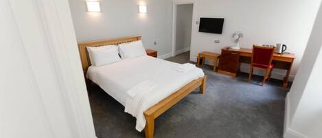 A bedroom with a wooden bed, a desk, a chair, and a TV on the wall.