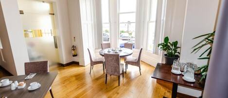 Een hotelkamer met een ronde eettafel, vier stoelen, een potplant en een raam met gordijnen.