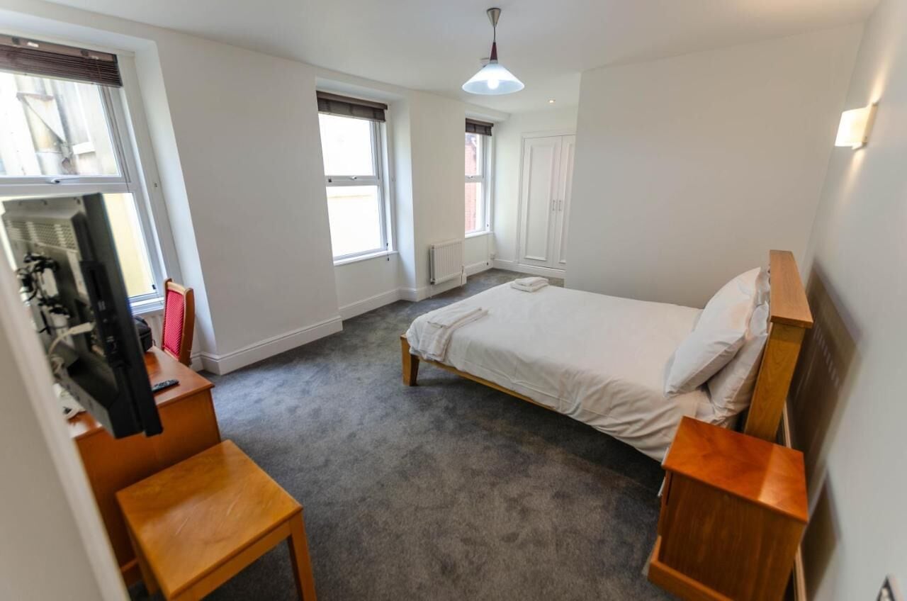 Ein Schlafzimmer mit einem Einzelbett, einem Holztisch, einem Stuhl und einem Fernseher.