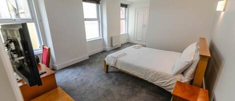 Un dormitorio con una cama individual, un escritorio de madera, una silla y un televisor.