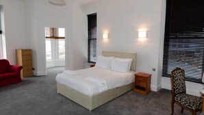 A bedroom with a bed, bedside tables, a chair, a dresser, and a window with blinds. - Opul Boutique (Douglas)